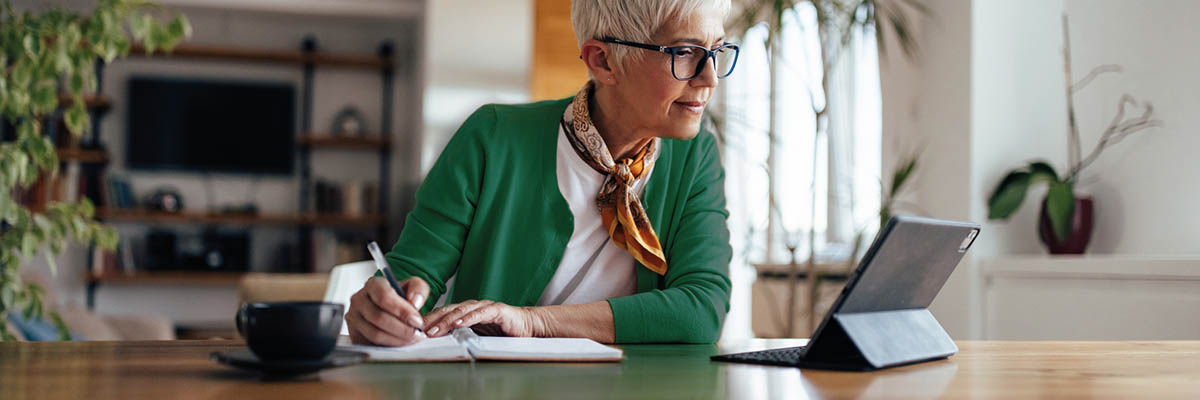 Person sitting at table with tablet device, pen and notepad