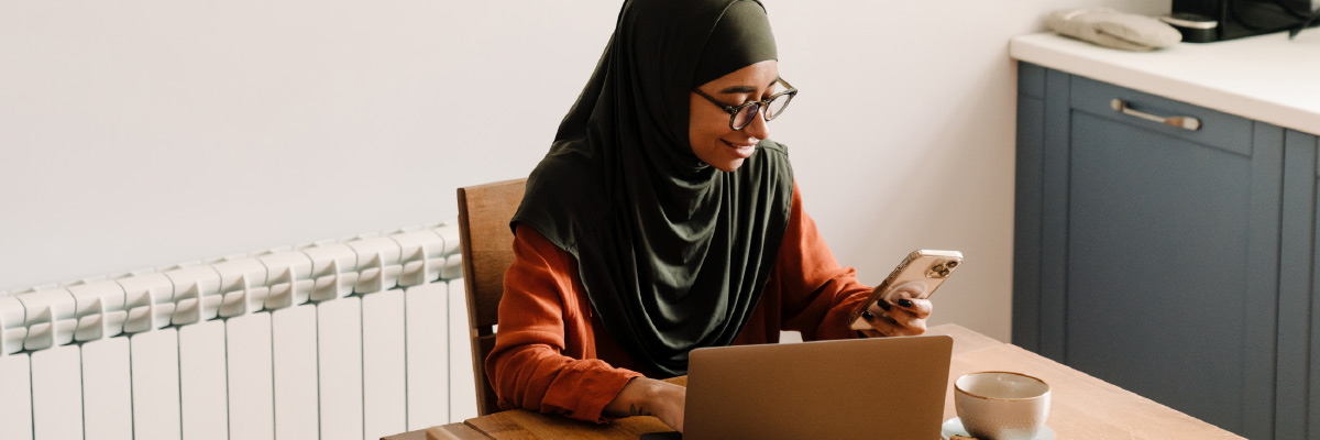 Person holding mobile sat at table with laptop and cup