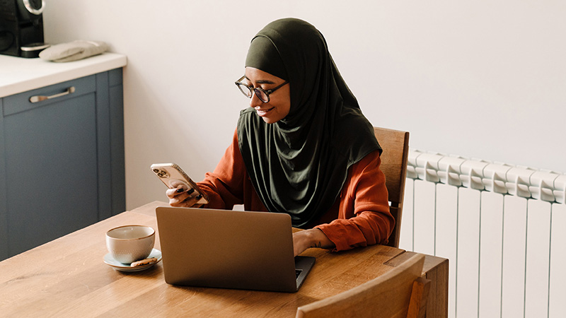 Person holding mobile sat at table with laptop and cup